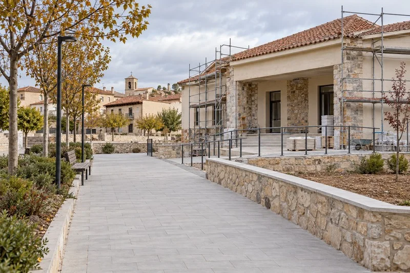 Pavimento peatonal junto a un edificio municipal en obras, en una plaza de un pueblo.