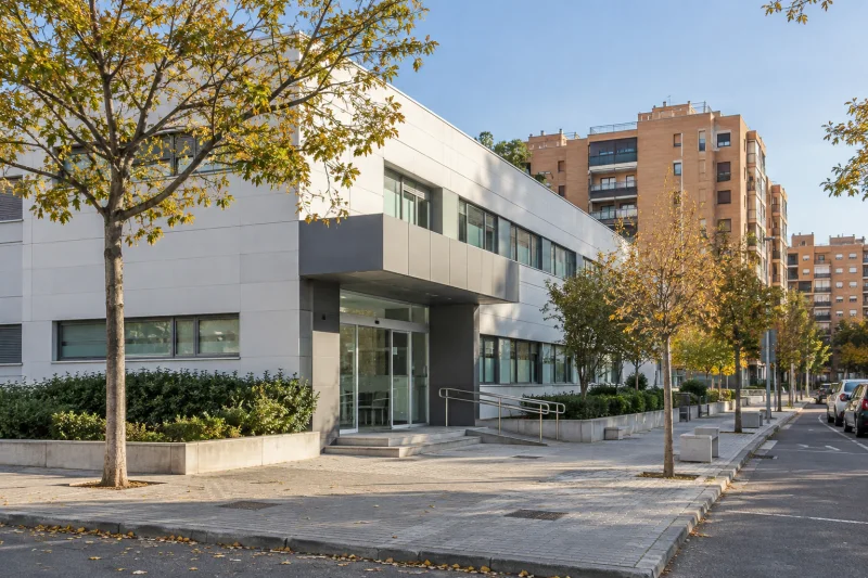 Fachada de un centro de atención primaria en un barrio residencial, con acceso acristalado y árboles en la acera.