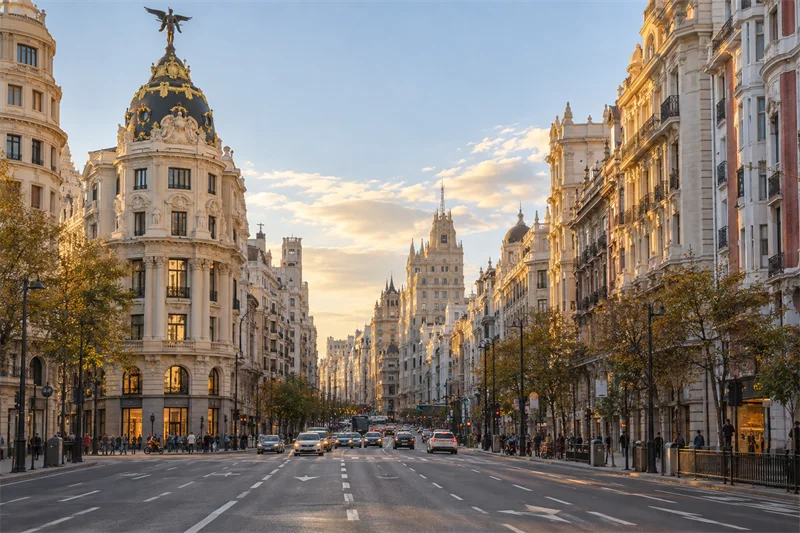 Vista de Gran Vía de Madrid al atardecer, con sus edificios históricos y tráfico en la calzada.