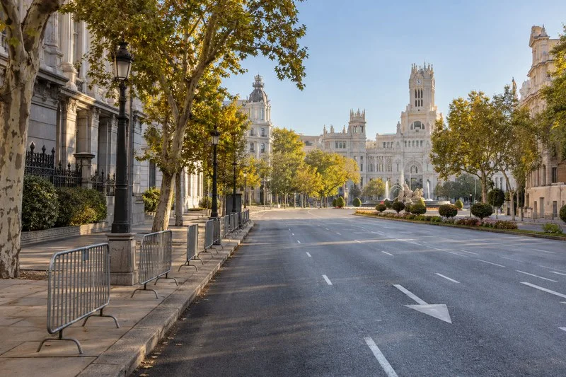 Vista del paseo del Prado en Madrid con vallas provisionales en la acera y edificios del entorno de Cibeles al fondo.